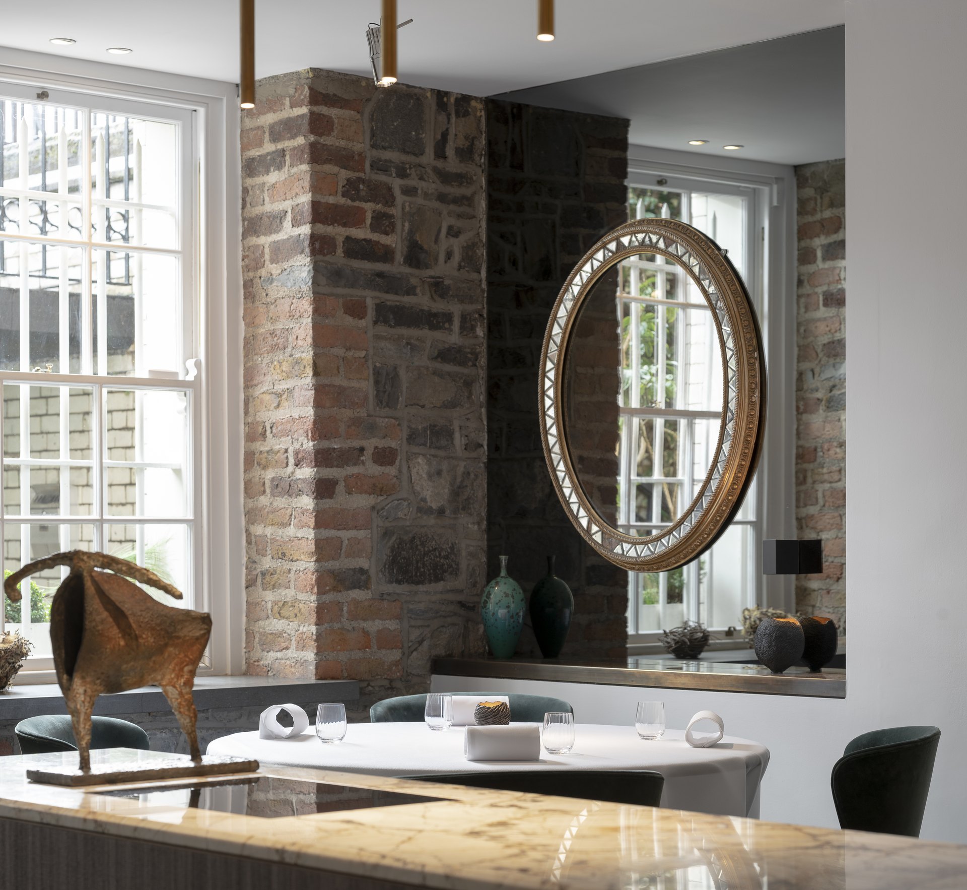 A corner of Chapter One: old brick and stone walls, a gilt oval mirror, Georgian sash windows and a bronze sculpture