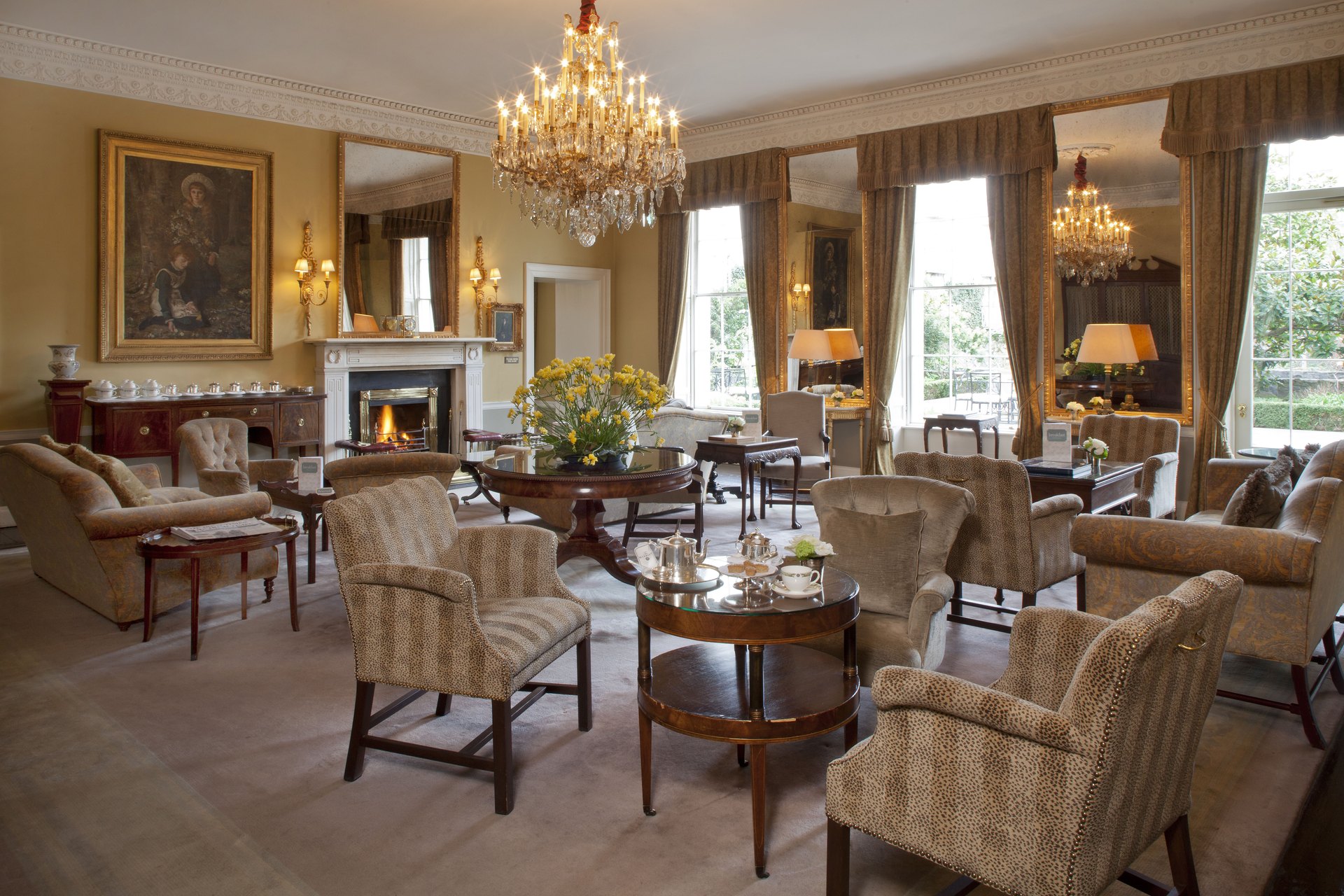 The Drawing Rooms at The Merrion: a crystal chandelier, a lit fire, armchairs and tea set out on low tables