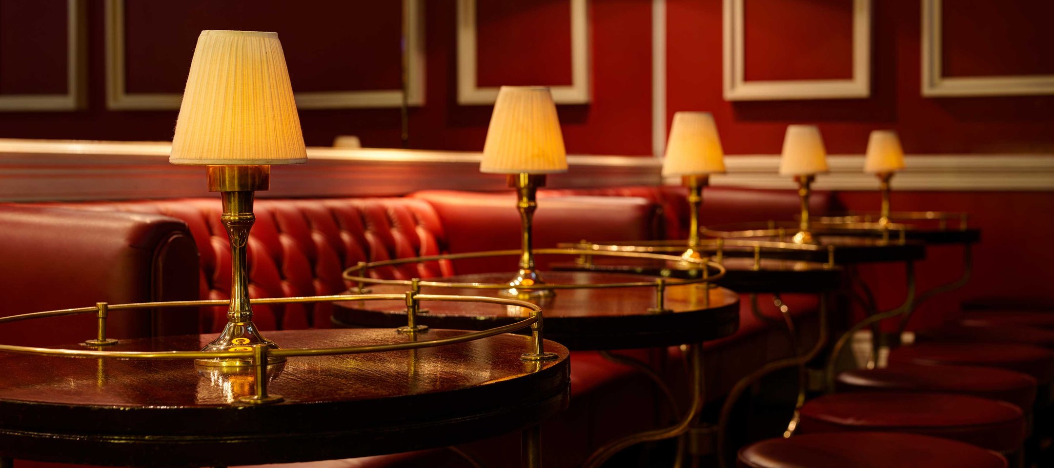 The Horseshoe Bar at The Shelbourne: red leather banquettes, brass-railed tables and pleated lamps against red walls
