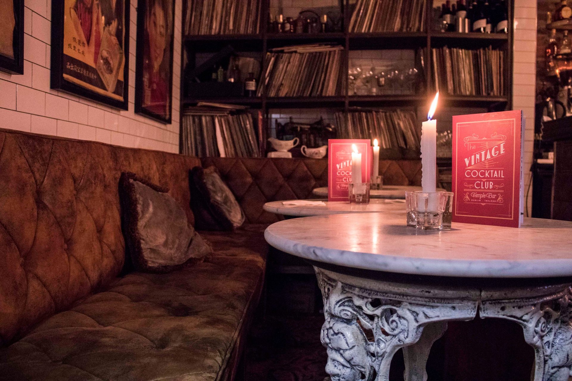 A candlelit marble table and buttoned leather banquette at Vintage Cocktail Club, with shelves of records behind
